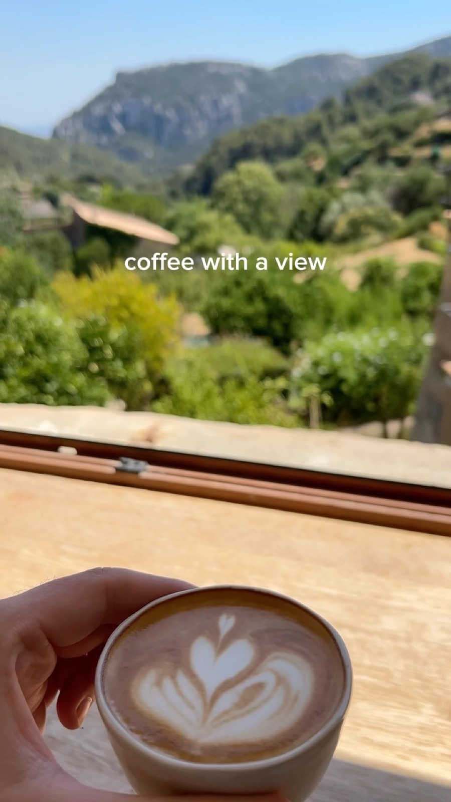 Coffee held up against the window, the Tramuntana mountains beyond